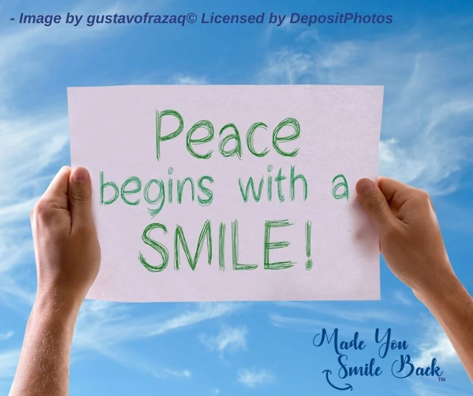 Image of a sign being held up in the sky displaying "Peace Begins with a Smile" by Made You Smile Back